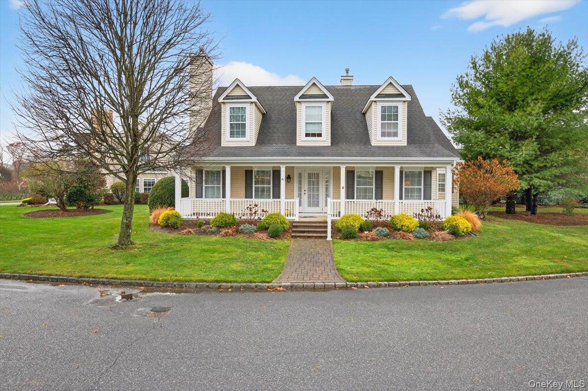 New england style home featuring a chimney, a front yard, and covered porch