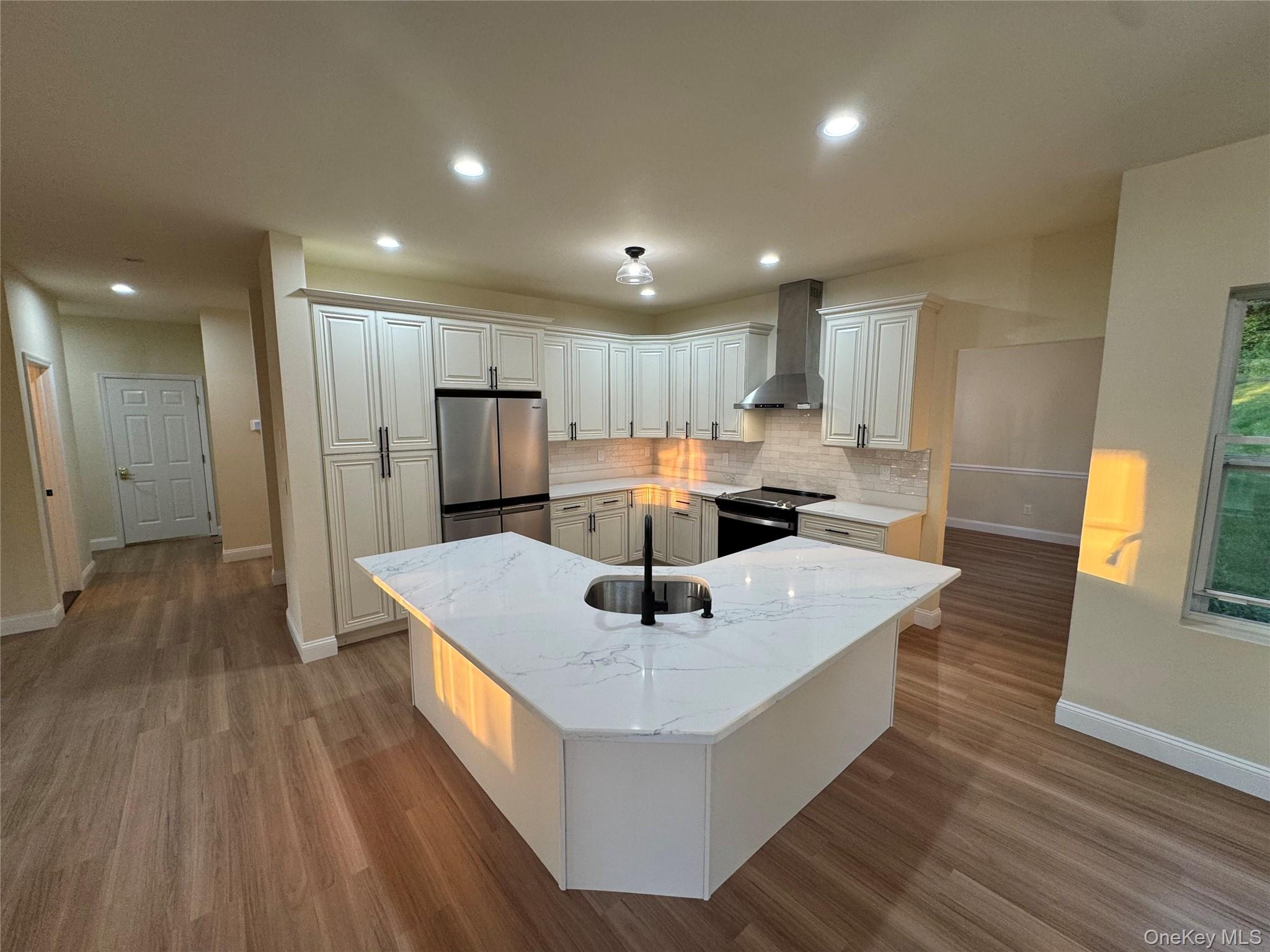 Kitchen with freestanding refrigerator, light stone countertops, black range with electric stovetop, decorative backsplash, and wall chimney exhaust hood