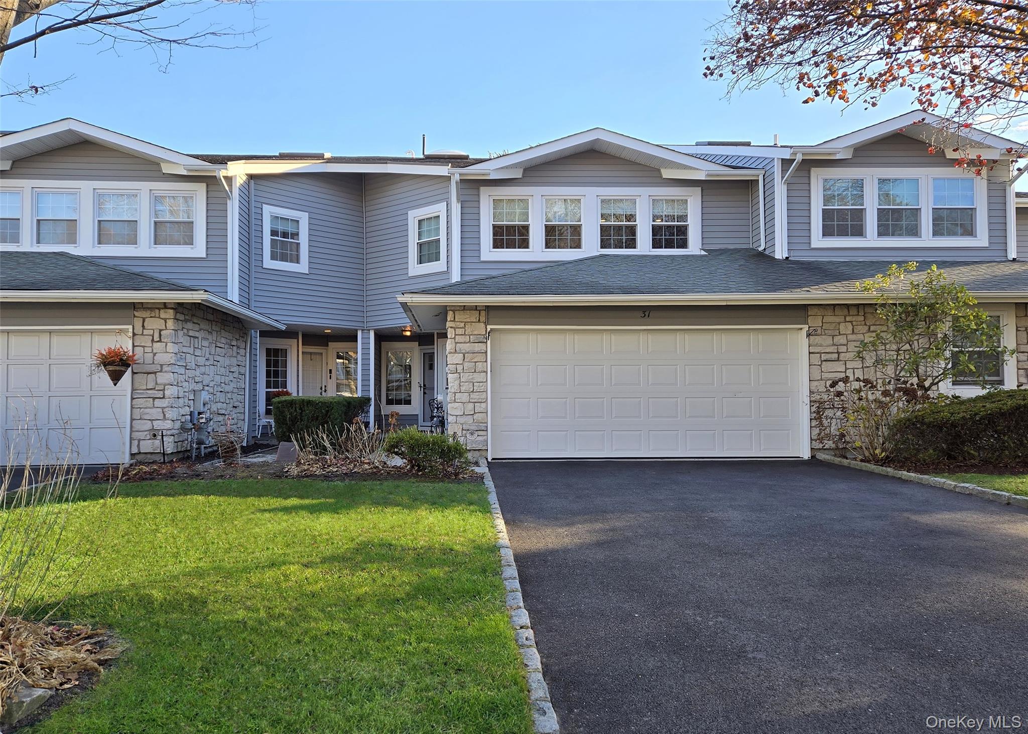 Traditional home featuring stone siding, asphalt driveway, a front lawn, and a shingled roof