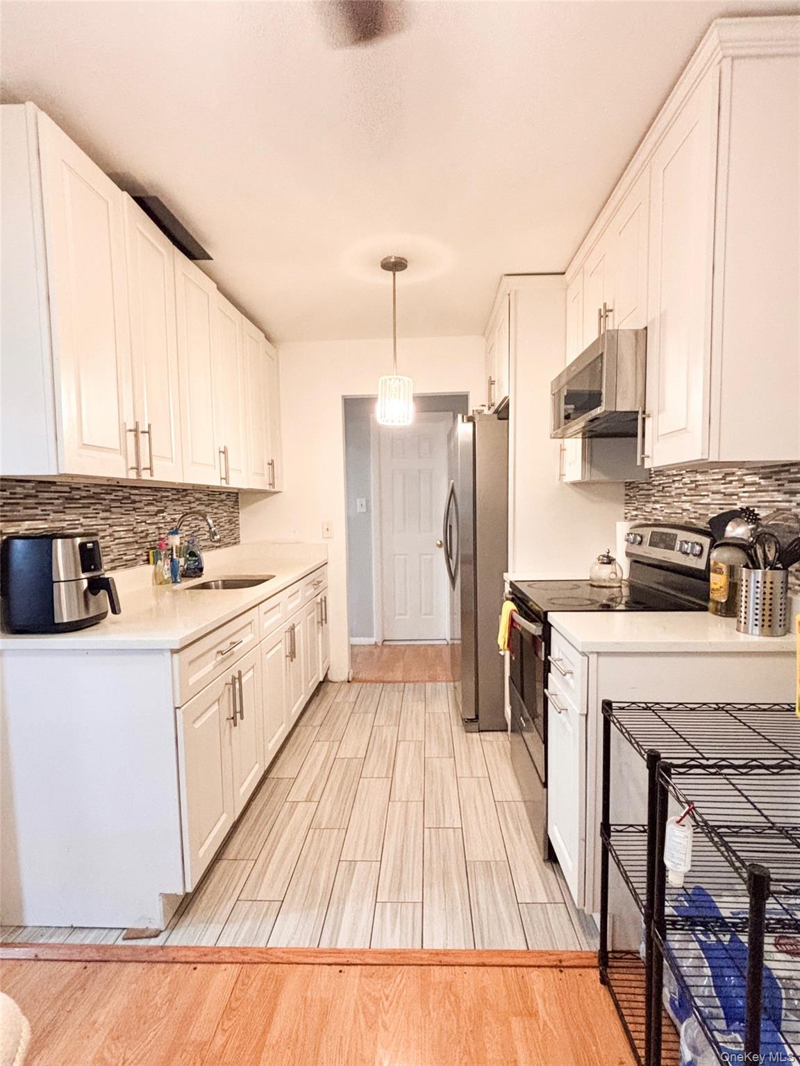 Kitchen featuring tasteful backsplash, stainless steel appliances, white cabinetry, and decorative light fixtures