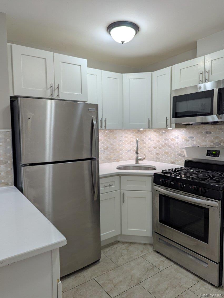 Kitchen featuring appliances with stainless steel finishes, decorative backsplash, white cabinets, and light stone countertops