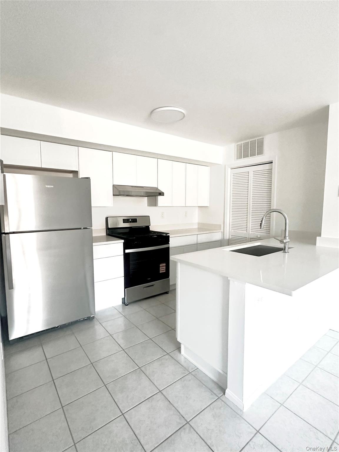 Kitchen with stainless steel appliances, white cabinets, light tile patterned floors, and under cabinet range hood