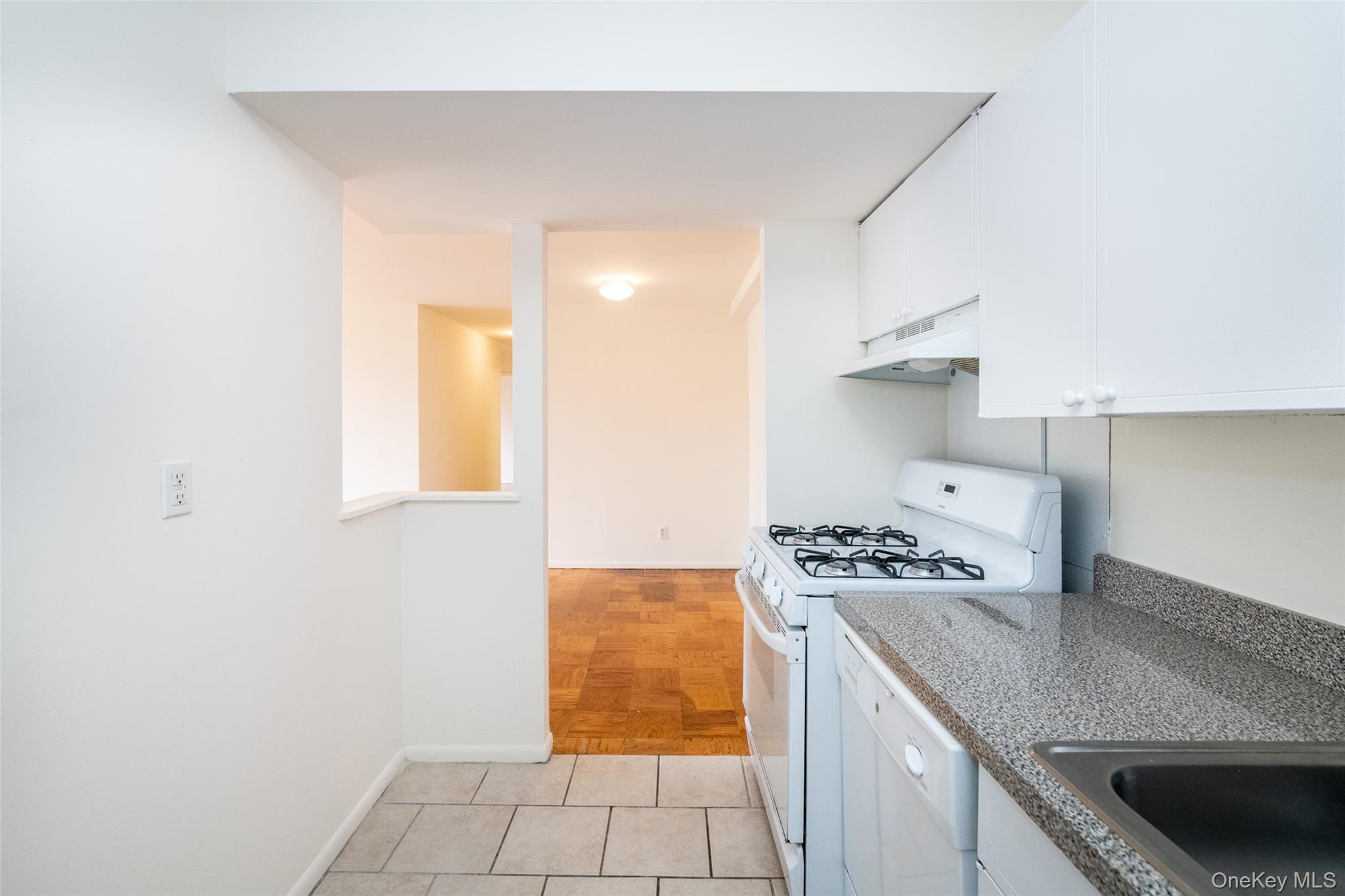 Kitchen featuring white appliances, white cabinets, under cabinet range hood, and light tile patterned floors