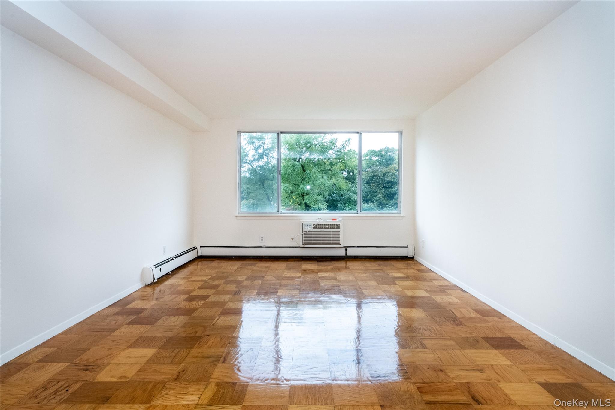 Unfurnished room featuring baseboard heating and an AC wall unit