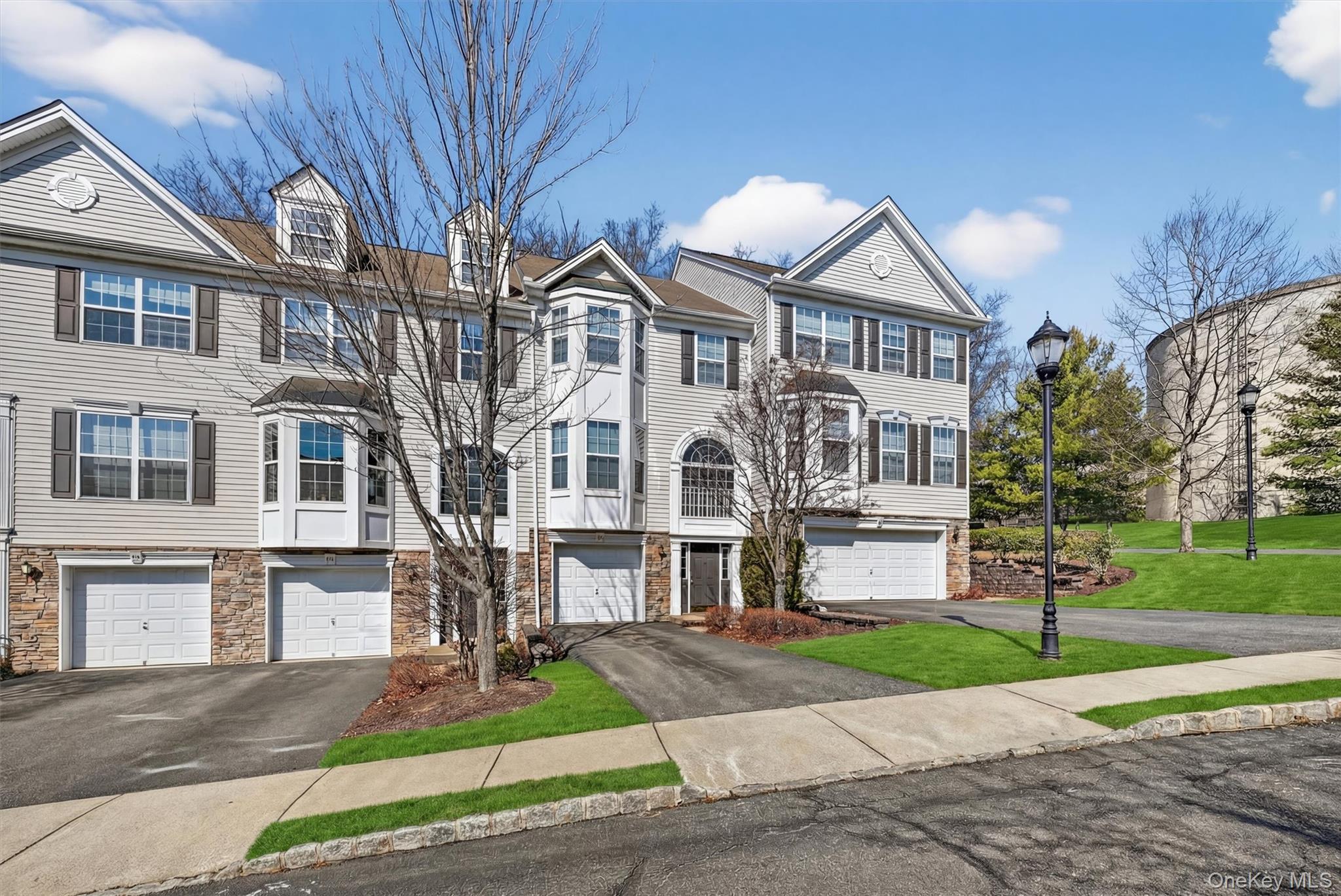 Townhouse with stone siding, driveway, and an attached garage