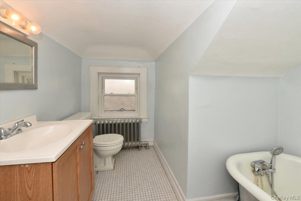 Full bathroom with vanity, tile patterned flooring, toilet, radiator, and a freestanding bath