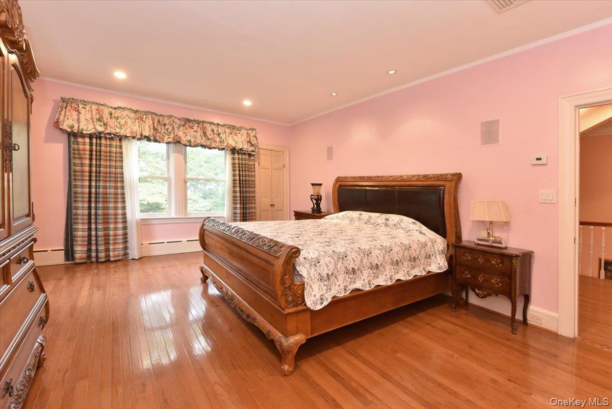 Bedroom with baseboard heating, crown molding, wood-type flooring, and baseboards