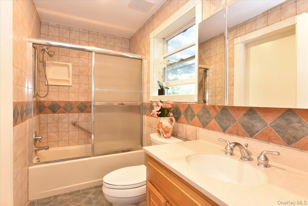 Bathroom featuring tile patterned flooring, toilet, vanity, and bath / shower combo with glass door