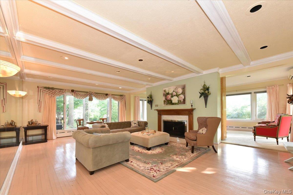 Living area featuring a fireplace, light wood-style floors, crown molding, and beam ceiling