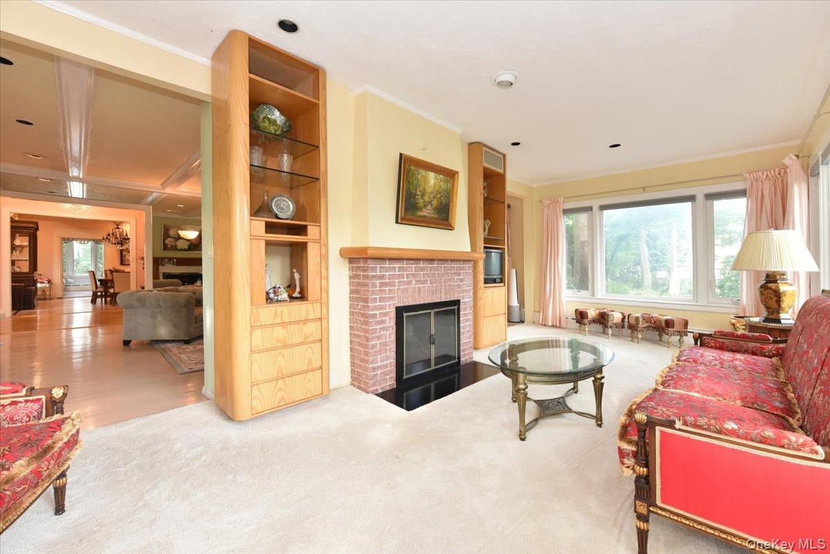 Carpeted living room with a fireplace, built in shelves, and ornamental molding