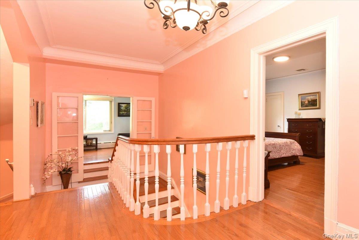 Corridor with crown molding, wood finished floors, a notable chandelier, and an upstairs landing