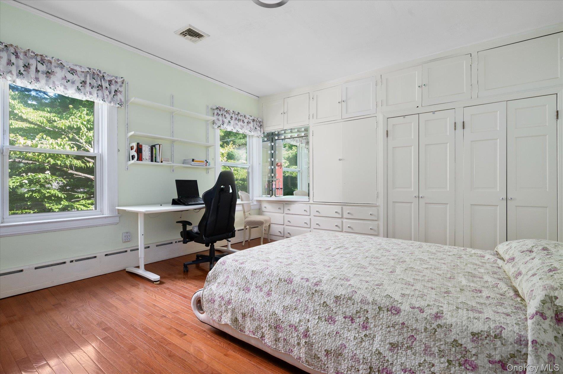 Bedroom with light wood-style floors, visible vents, and baseboard heating