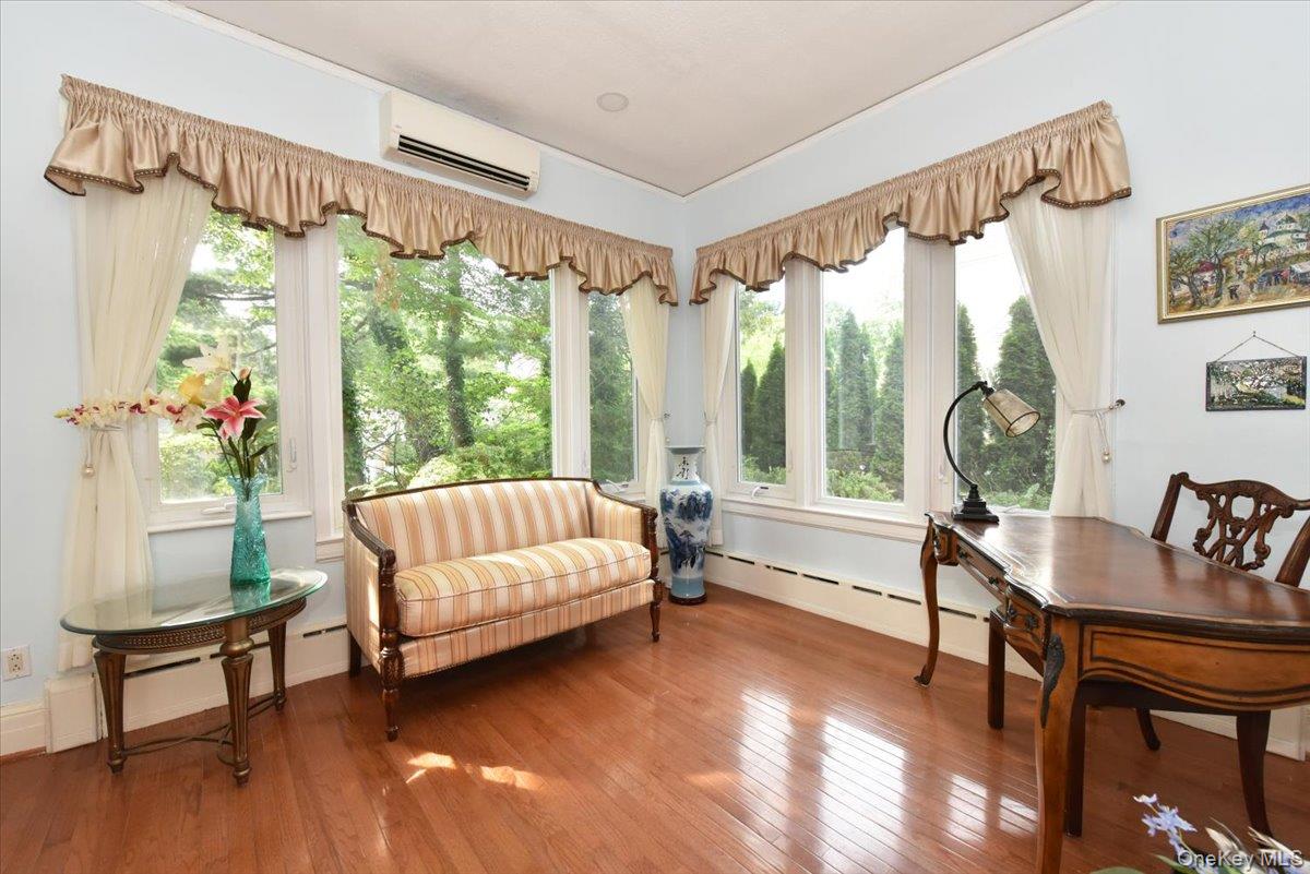 Living area with a wealth of natural light, a wall mounted AC, baseboard heating, and hardwood / wood-style flooring