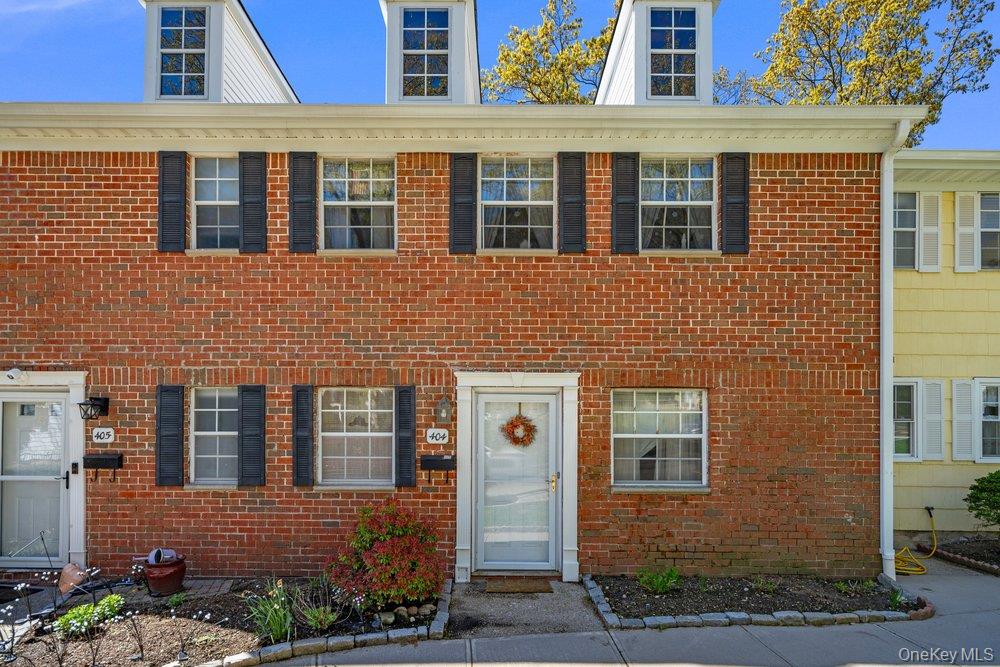 Brick townhouse exterior featuring white trim, black shutters, and a manicured planting bed