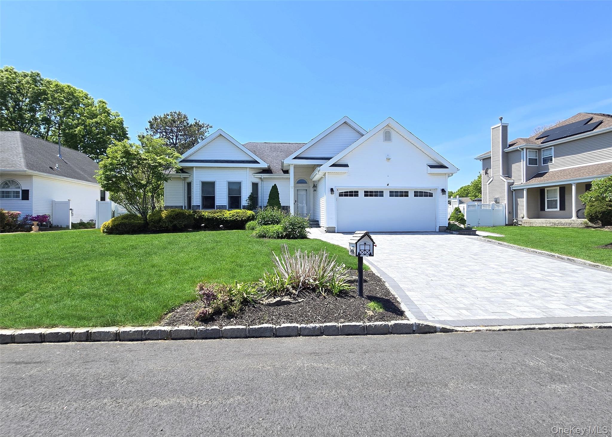 Ranch-style residence featuring a white exterior, a paver driveway, and a two-car garage