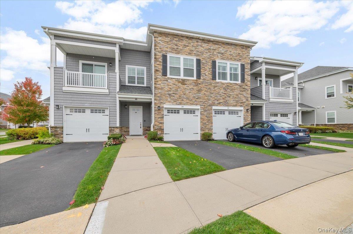 View of front facade with stonesiding, a balcony, driveway,and a garage