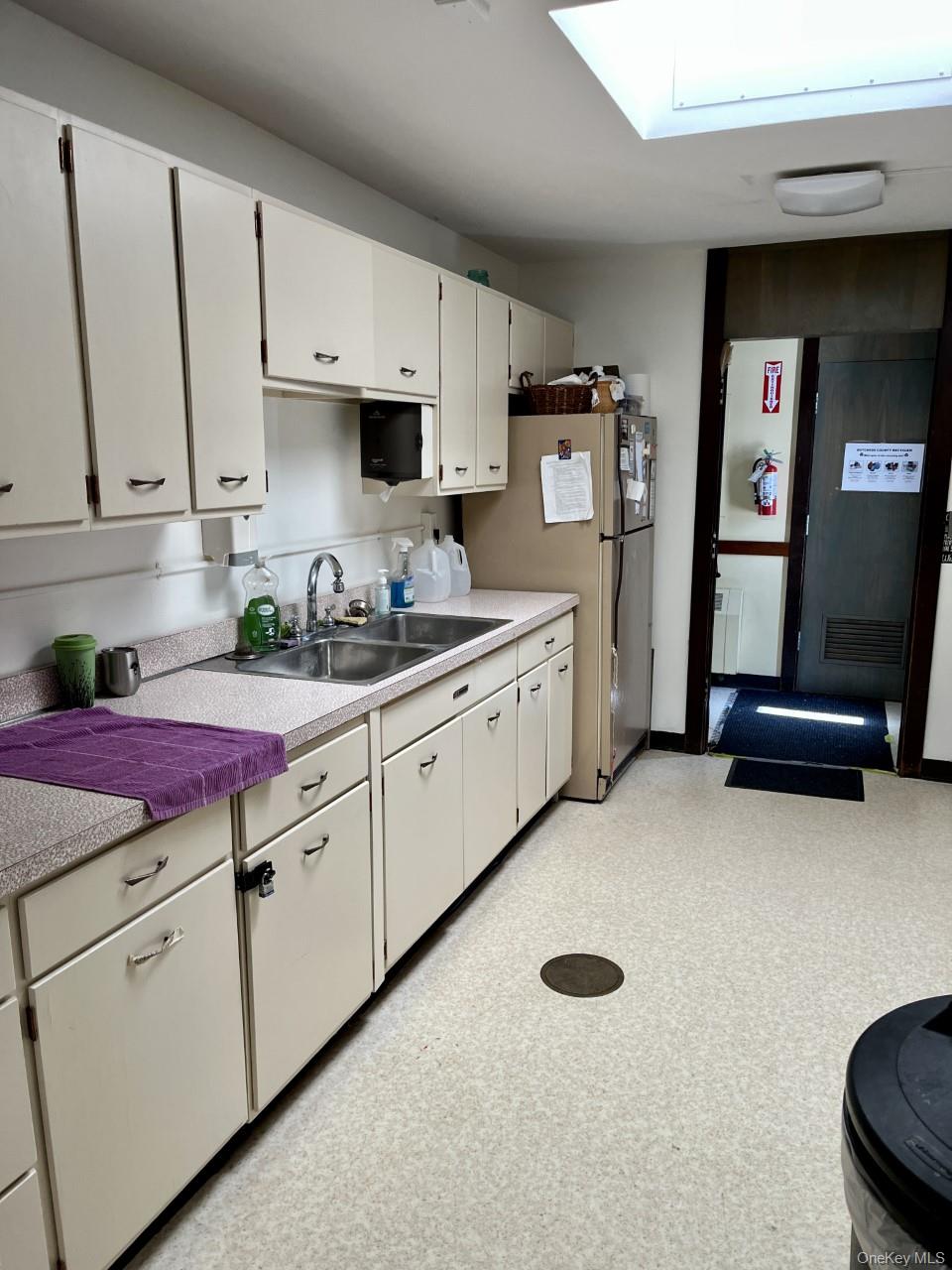 Kitchen featuring a sink, light countertops, freestanding refrigerator, a skylight, and white cabinetry