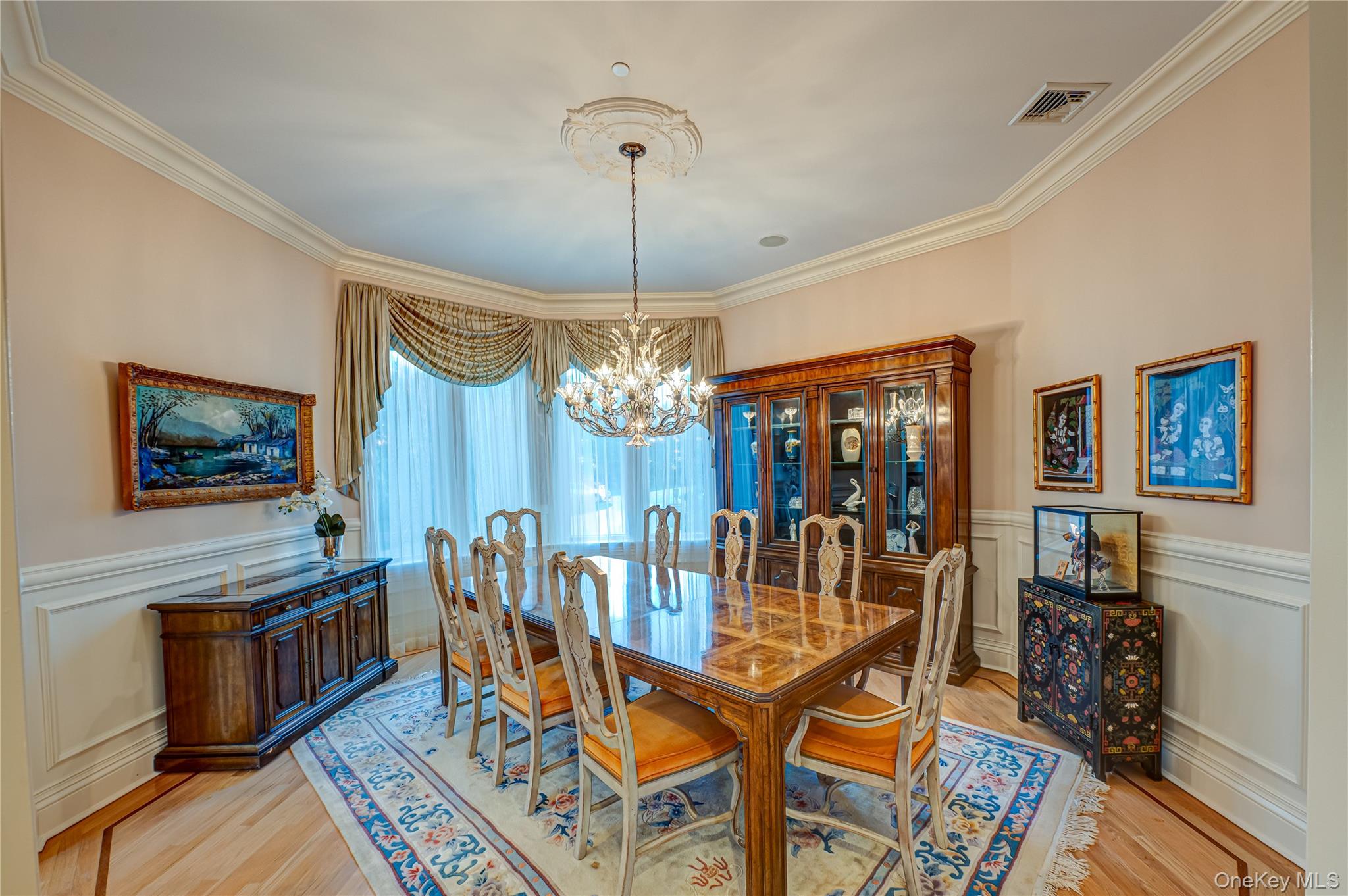 Dining room with visible vents, crown molding, light wood-type flooring, a wainscoted wall, and an inviting chandelier