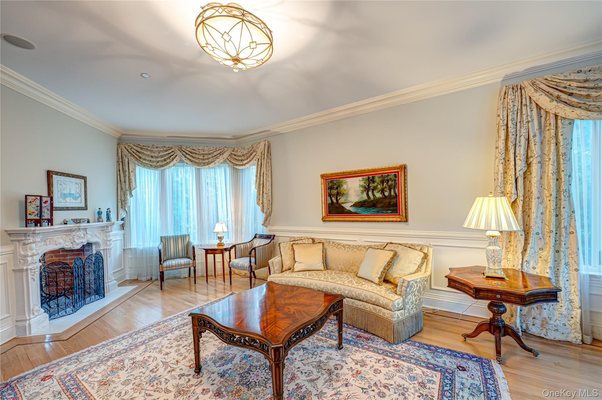 Living room with crown molding, a fireplace with raised hearth, wainscoting, and wood finished floors