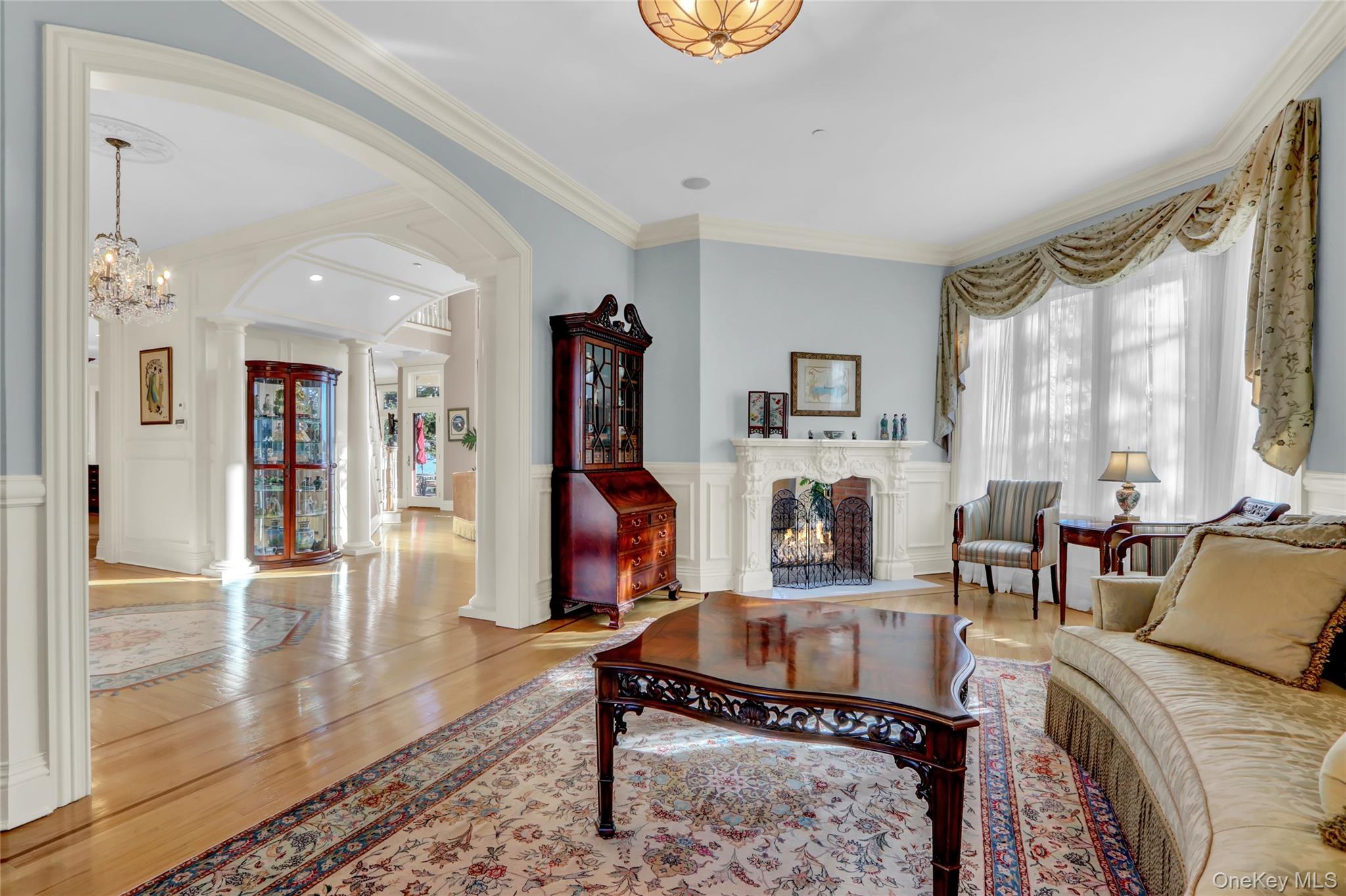 Living room featuring decorative columns, wood finished floors, a lit fireplace, and crown molding