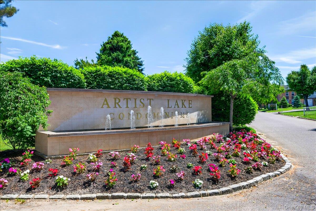 Artist Lake Condominiums entrance sign featuring a stone facade with integrated fountains, vibrant seasonal plantings, manicured shrubbery, and mature trees