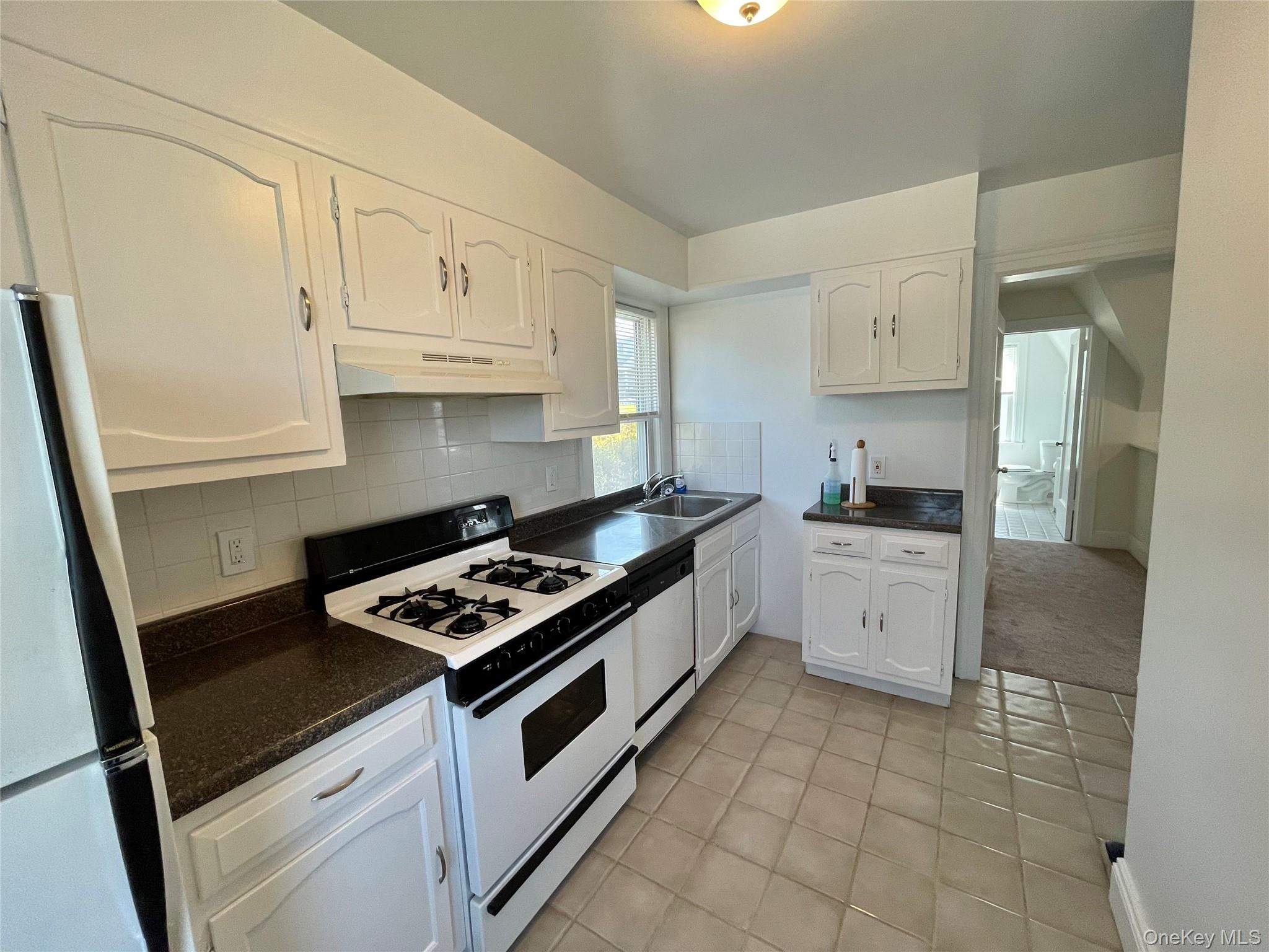 Kitchen with a sink, white cabinetry, white appliances, under cabinet range hood, and light tile patterned floors