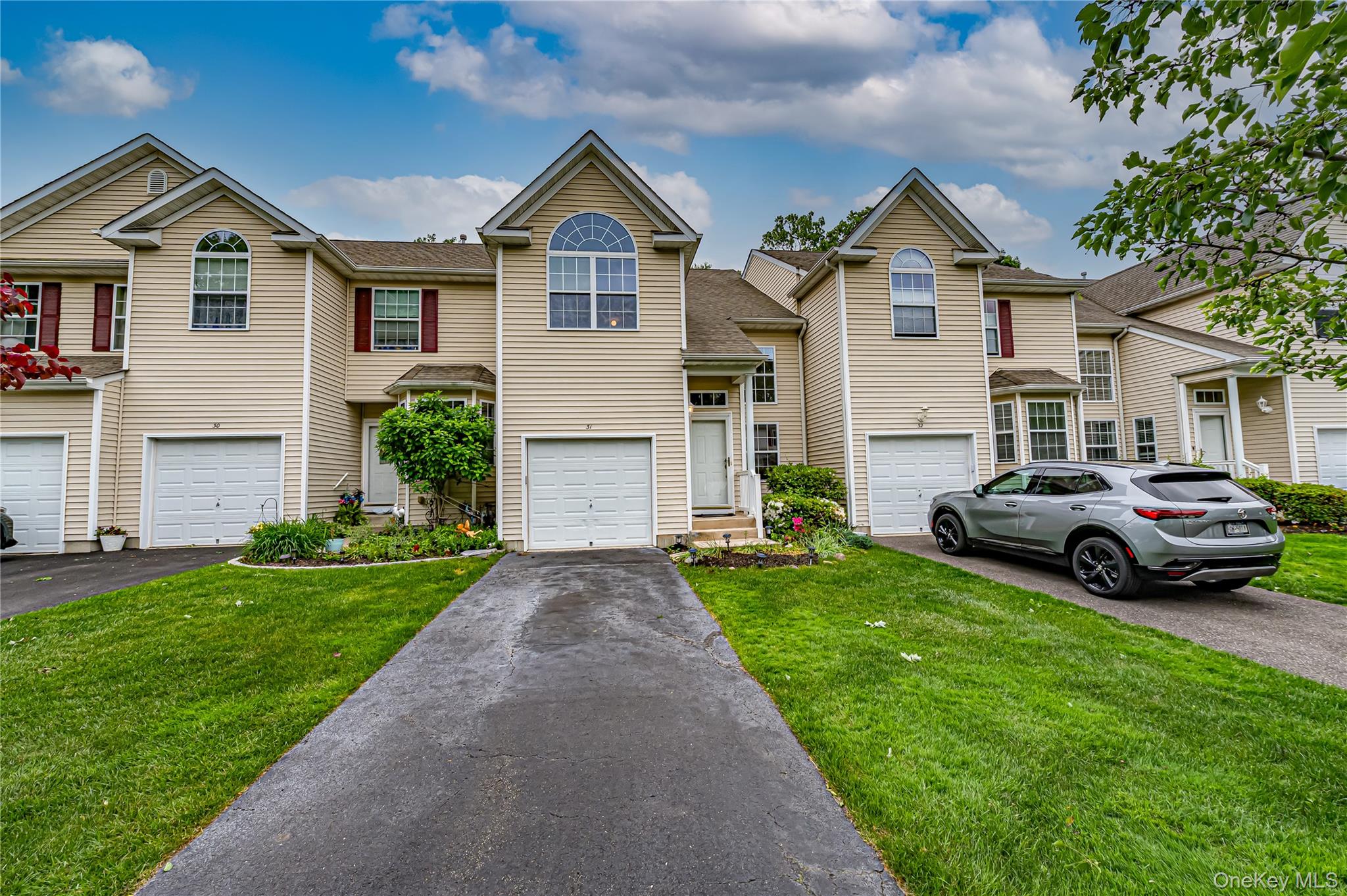 Townhome exterior featuring light beige siding, white garage doors, and arched windows
