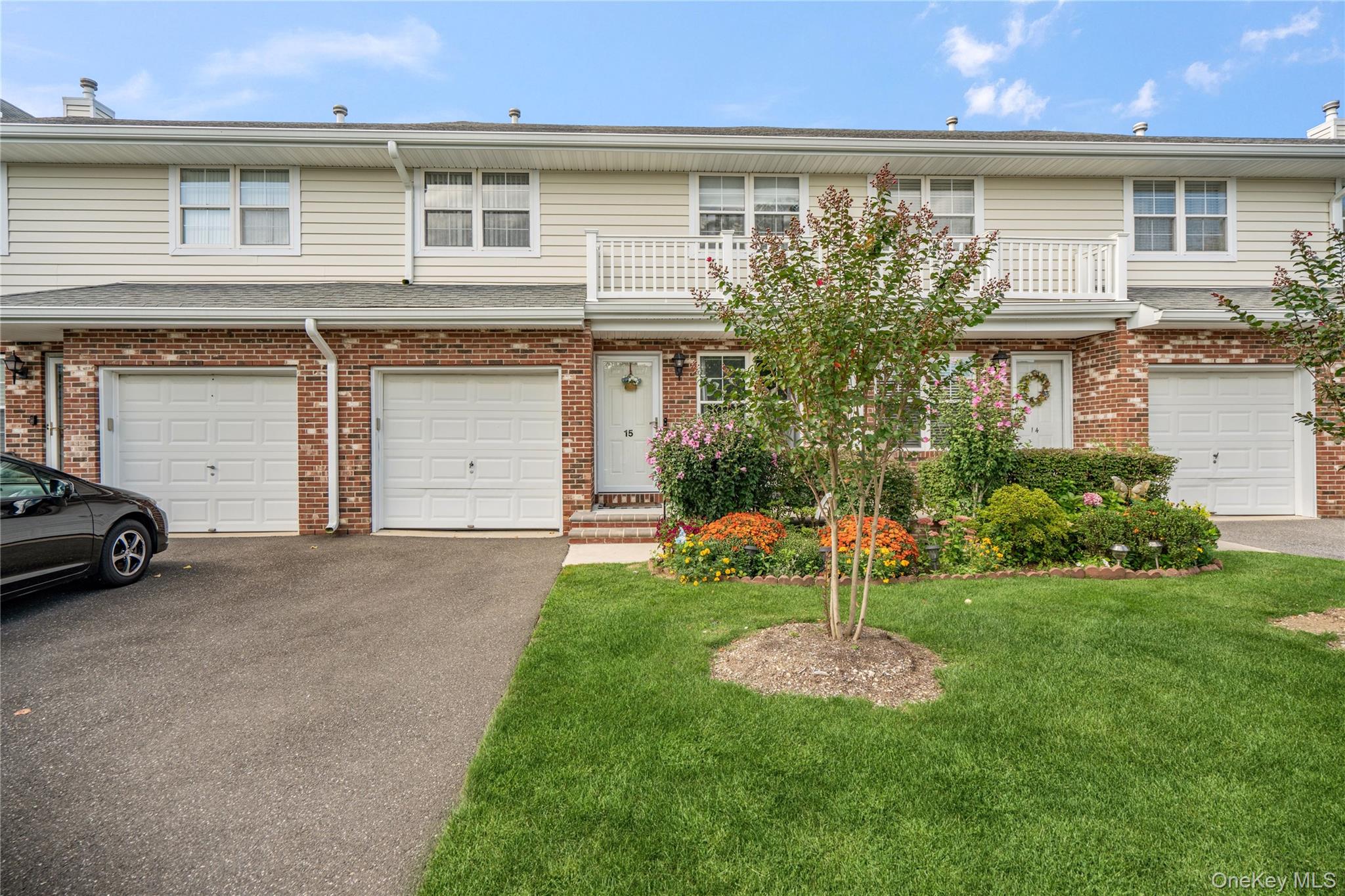 Brick lower facade with white siding, integrated two-car garage, manicured lawn, and established landscaping