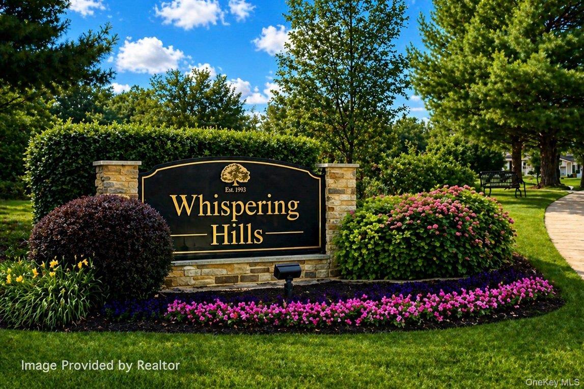 Stone and wood-finish community entrance sign, manicured landscaping with flowering shrubs, lush green lawn, and mature trees