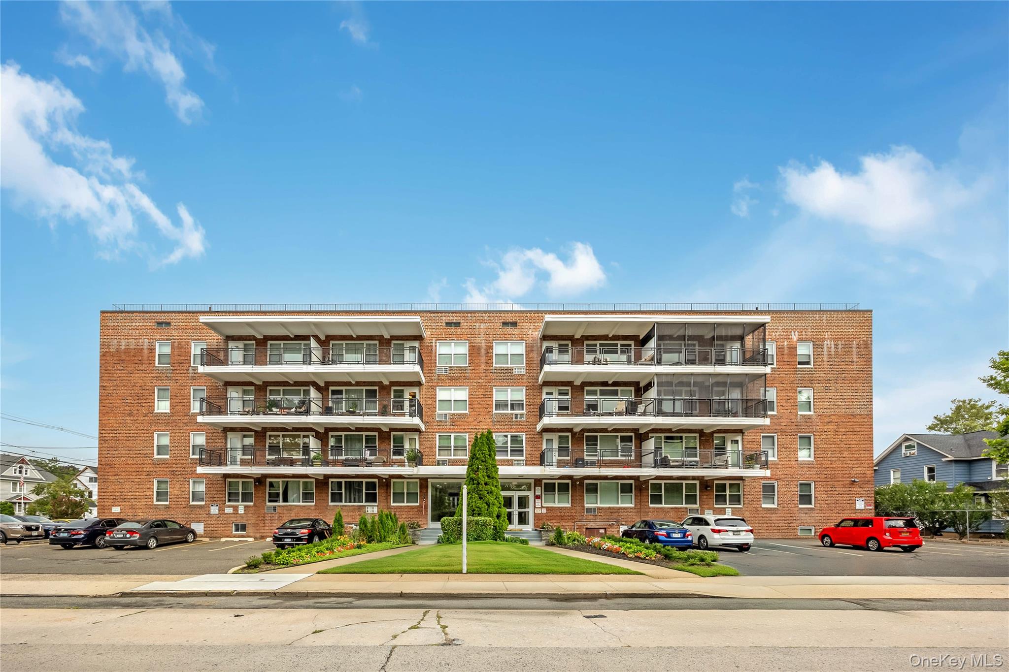 Brick exterior with multiple balconies, a manicured lawn, and dedicated surface parking